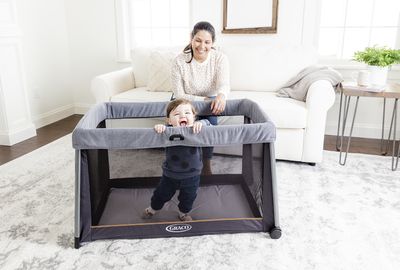 Graco FoldLite Travel Cot pictured with child playing in the cot with female carer looking on
