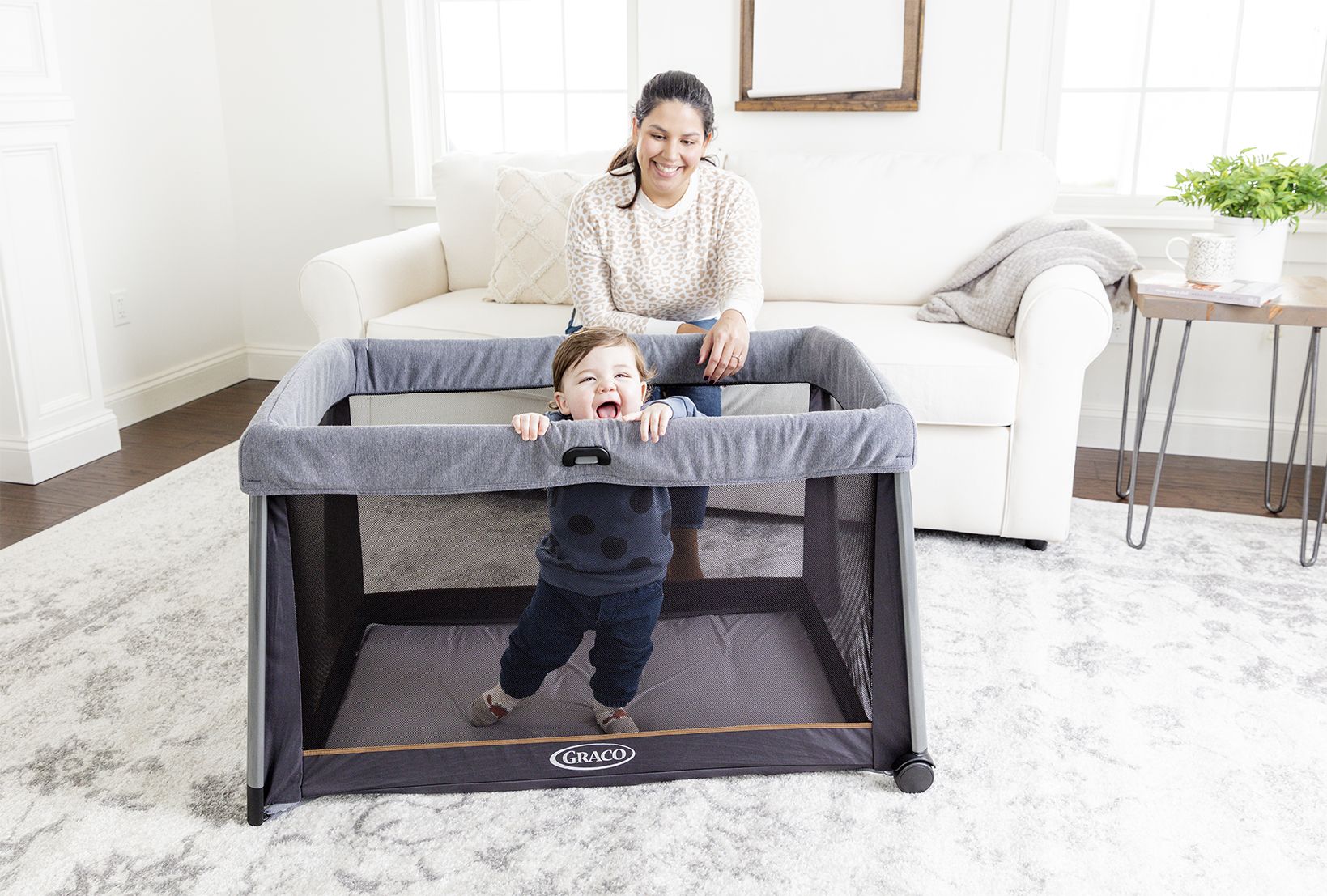 Graco FoldLite Travel Cot pictured with child playing in the cot with female carer looking on