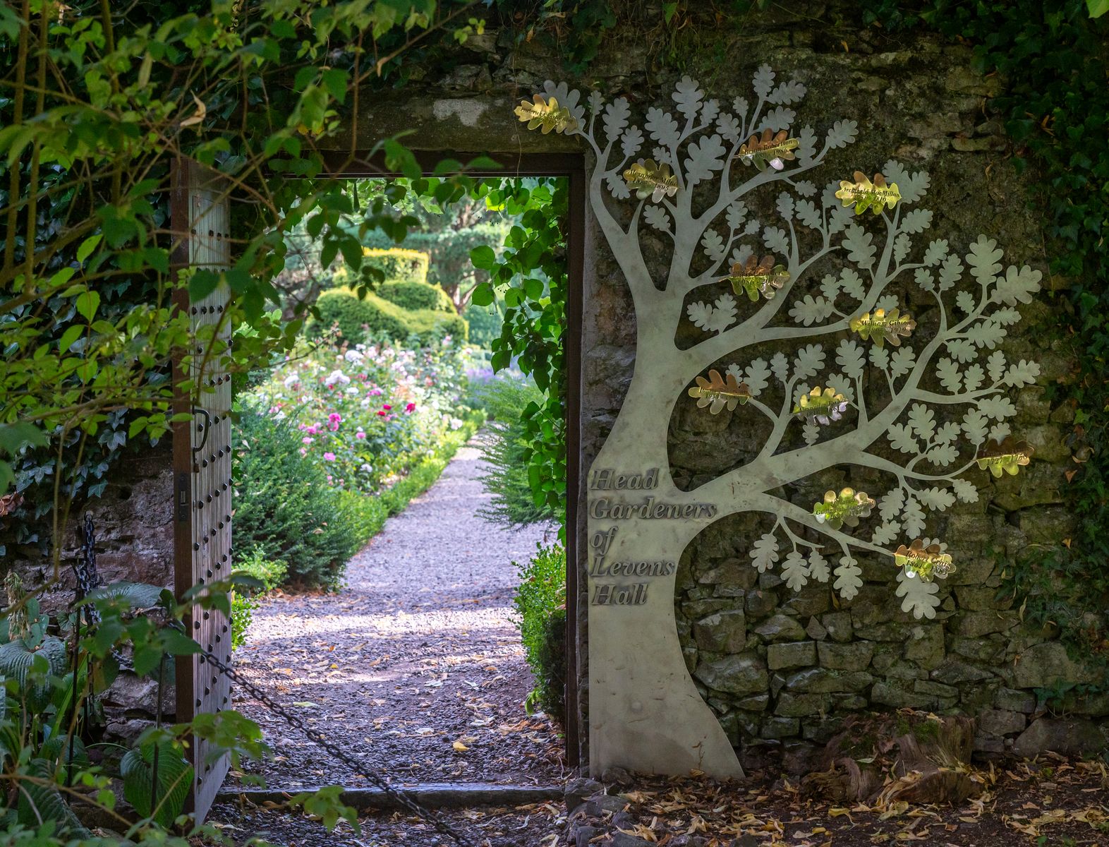 Looking through a gate from the Levens Hall garden, which now has the head gardeners' commemorative tree sculpture beside the gate.