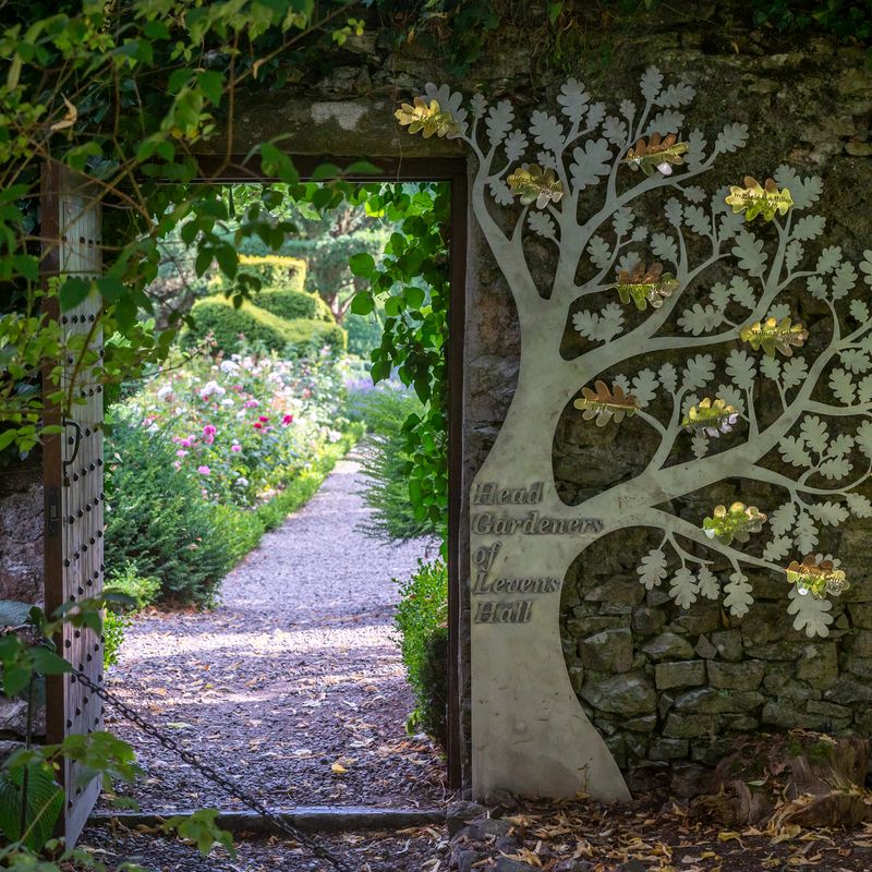 Looking through a gate from the Levens Hall garden, which now has the head gardeners' commemorative tree sculpture beside the gate.